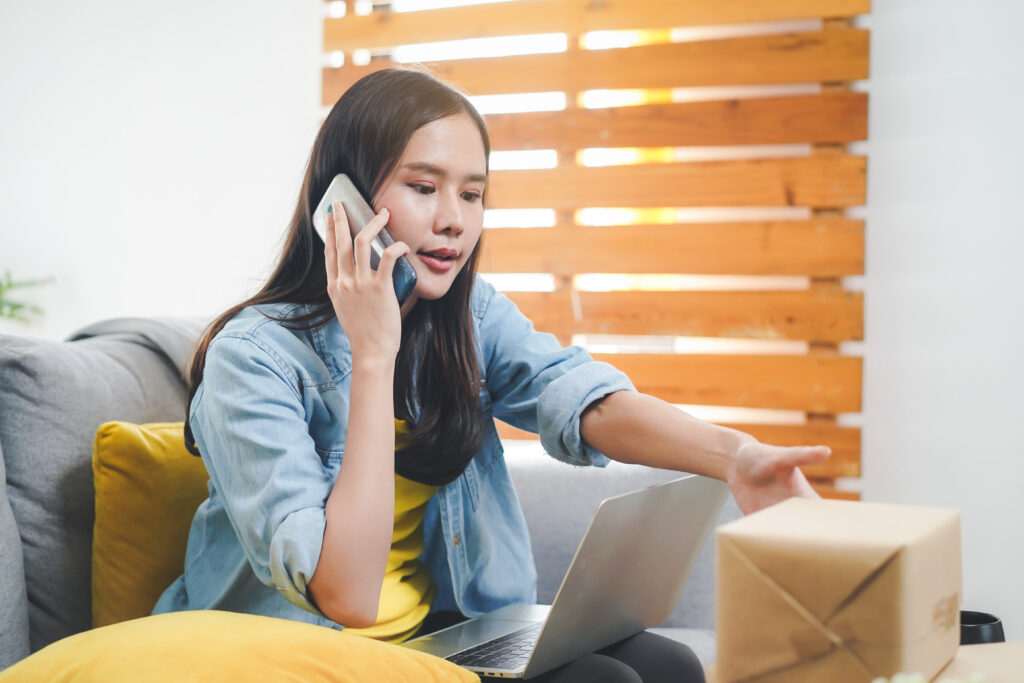 Asian woman sitting down at her laptop as she speaks to customer support about her package delivery