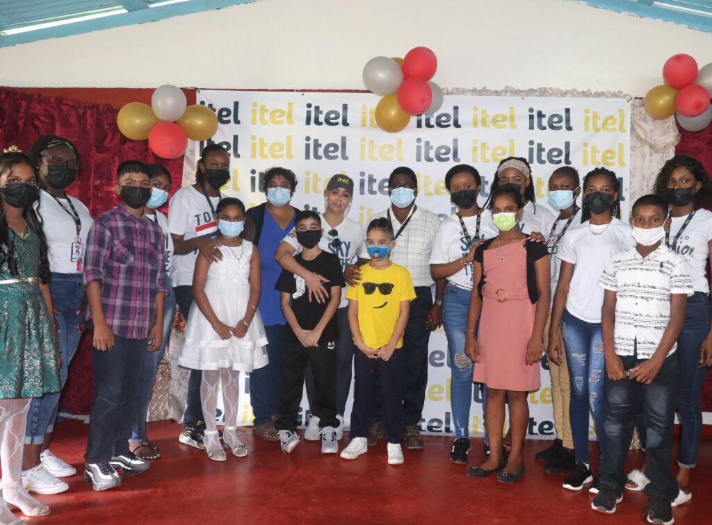 Image of itel representatives, Roslyn Braithwaite-Sears, Tiffany Higgins, Aisha D’Abreu, Sheriece Baker, Aallyah Adams, Ulex Dorris, Brittany Angus, Shivanie Pooran, and Stembiso Roberts, as they met with Wakenaam's local children and residents of all ages, for a special holiday luncheon hosted by the company at the island's community hall  (Wakenaam Island, Guyana).