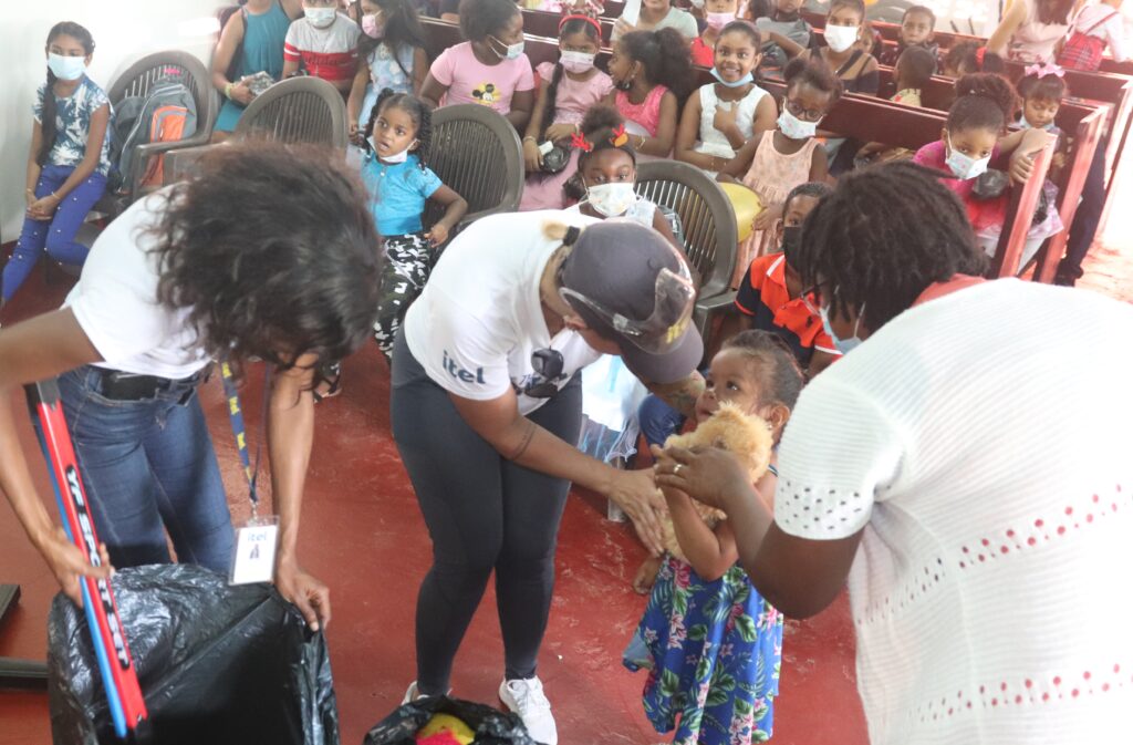 Image of itel team members handing out toys to each of the Wakenaam Island children who attended the company-sponsored holiday luncheon on December 18th, 2021. "It was the highlight of our trip,"  says Aisha D'Abreu, itel's Strategic Account Director, as she hands a teddy bear to a grateful little girl. 