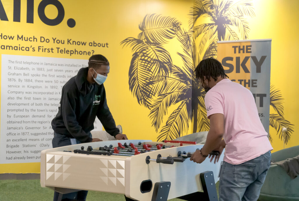 Image of two itel employees playing foosball in one of the CX company's iconic Chill Space rec rooms. A colorful mural with palm trees is seen in the background.