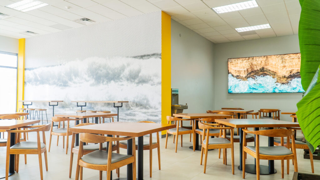 Image of the inside of itel's latest customer experience center in Jamaica. The main dining room and spacious cafeteria with a large mural, depicting crashing waves and the rugged coastlines of Jamaica, using a series of halftone patterns of varying weights, to create a newsprint-like, pop art effect.