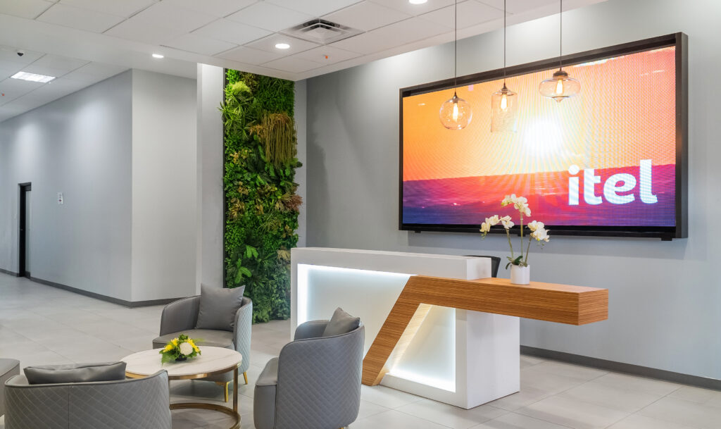 Image of itel's landmark building in Kingston, Jamaica. Interior main lobby with botanical walls, modern furnishings, elements of wood, large interactive TV screen and an ultramodern aesthetic that is revolutionizing contact center office design.