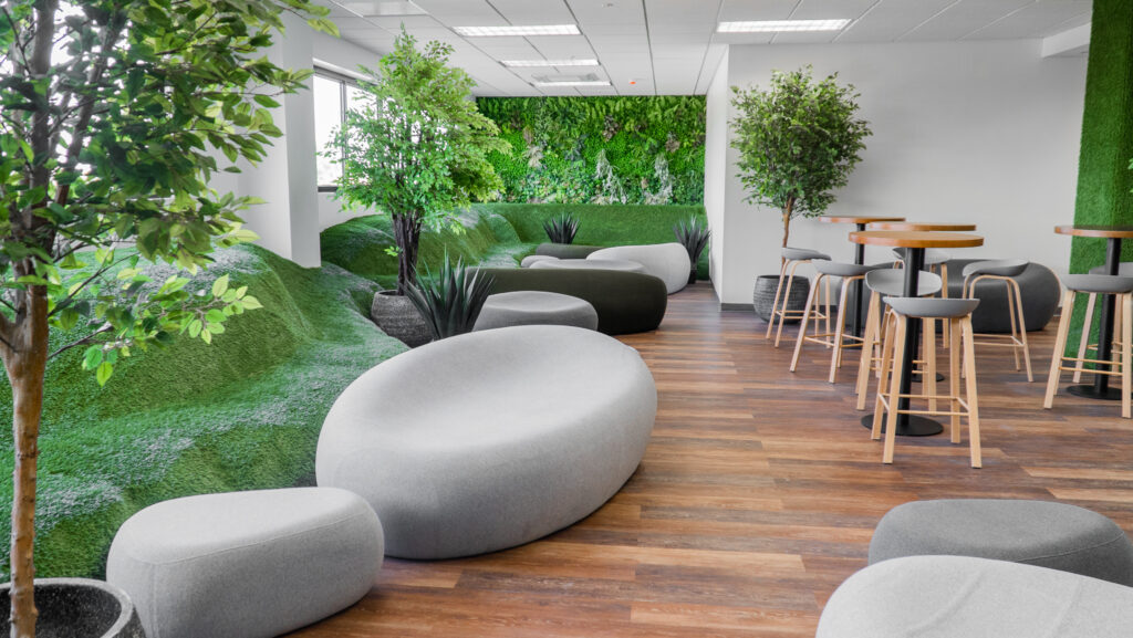 Image of the interior of itel's Chalmers building, a customer experience center in Kingston, Jamaica. The building's "chill spaces" or employee breakrooms, are designed to look like indoor parks, with hills of faux grass, wood floors, potted trees, a large botanical green wall, and unique chairs made to look like rocks.