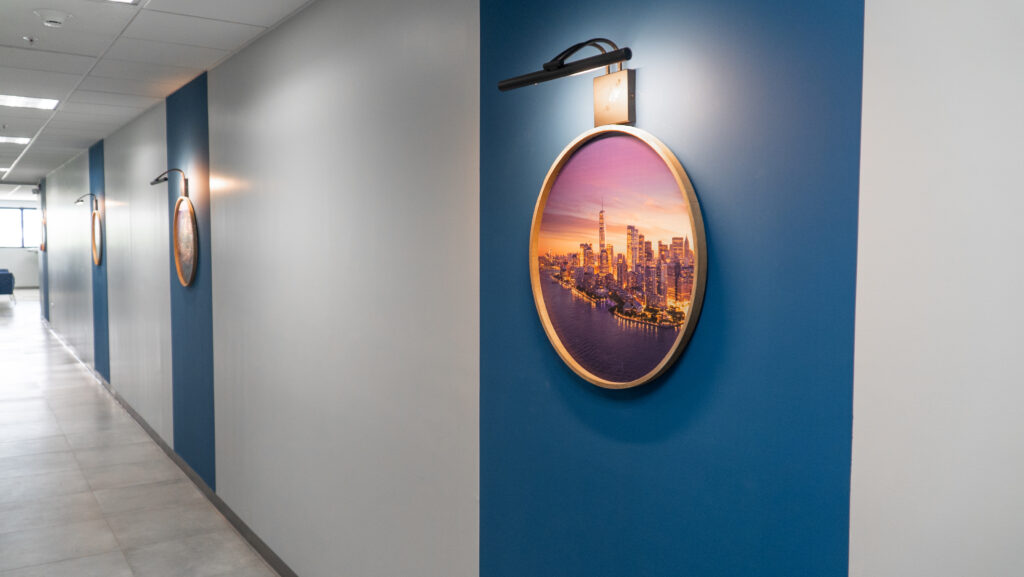 Image of one of Chalmers' floors,  dedicated to a top travel and hospitality client. Outside the production floor and meeting areas, the client's brand colors, a bright blue, are showcased in the hallways, with LED-lit artwork designed to look airplane windows or porthole "views" of various travel destinations. 